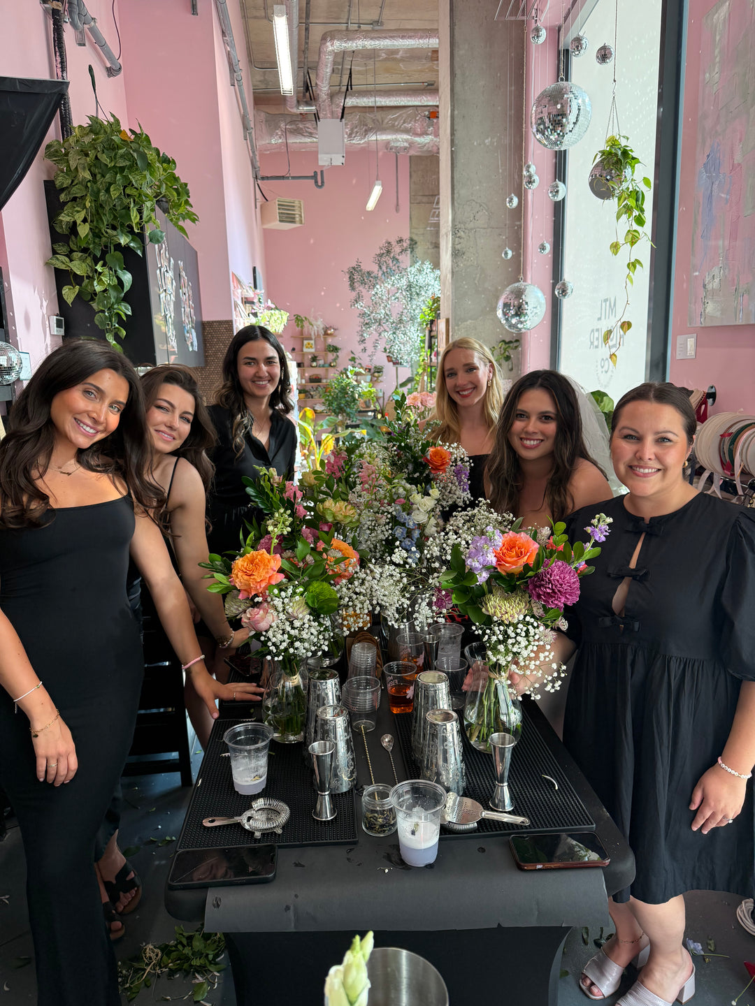 Group of women posing around a table with drinks and flowers in an indoor setting.