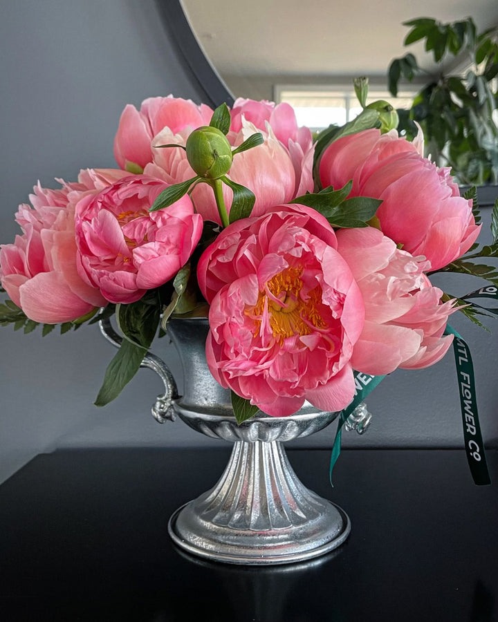 Pink flowers in a silver vase on a dark surface with a blurred background