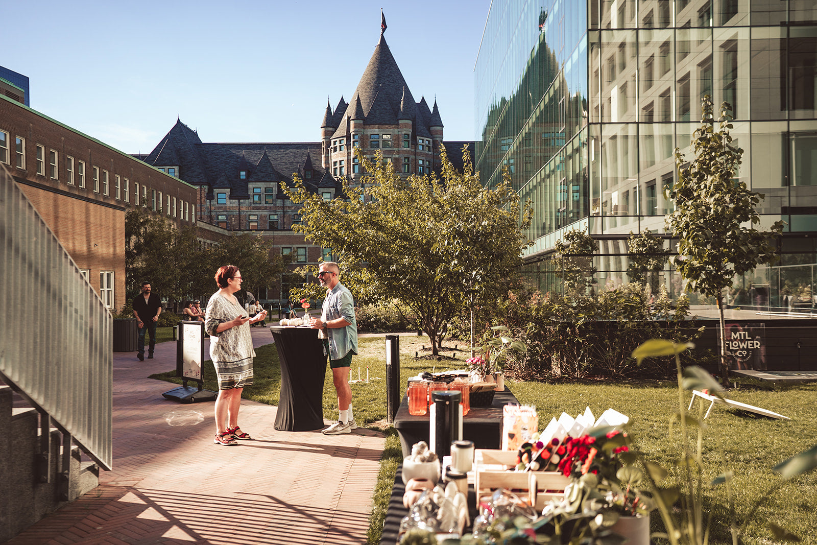 Two people standing on a sunlit outdoor patio with modern architecture in the background