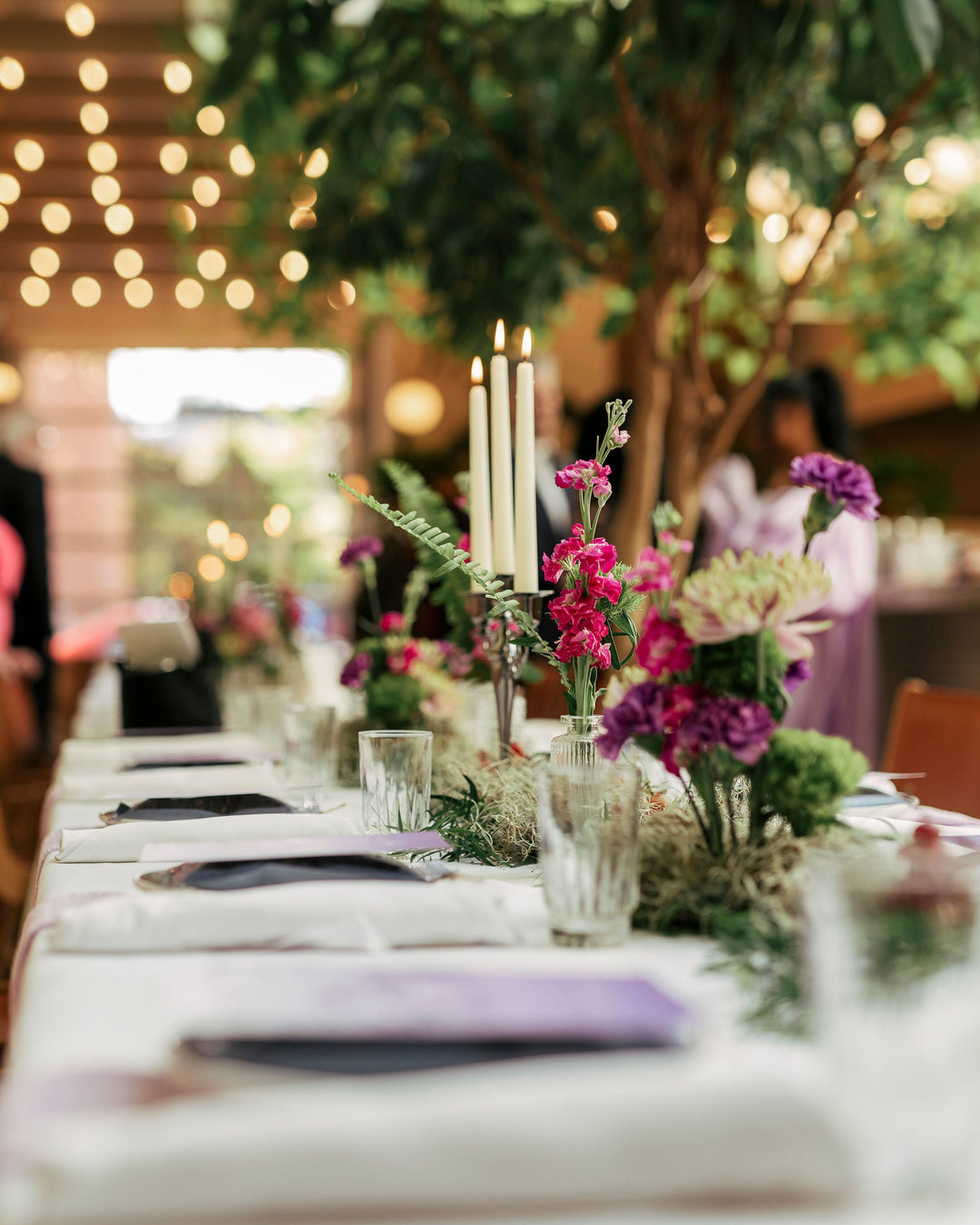 Decorative table setting with flowers and candles in an outdoor setting with string lights.