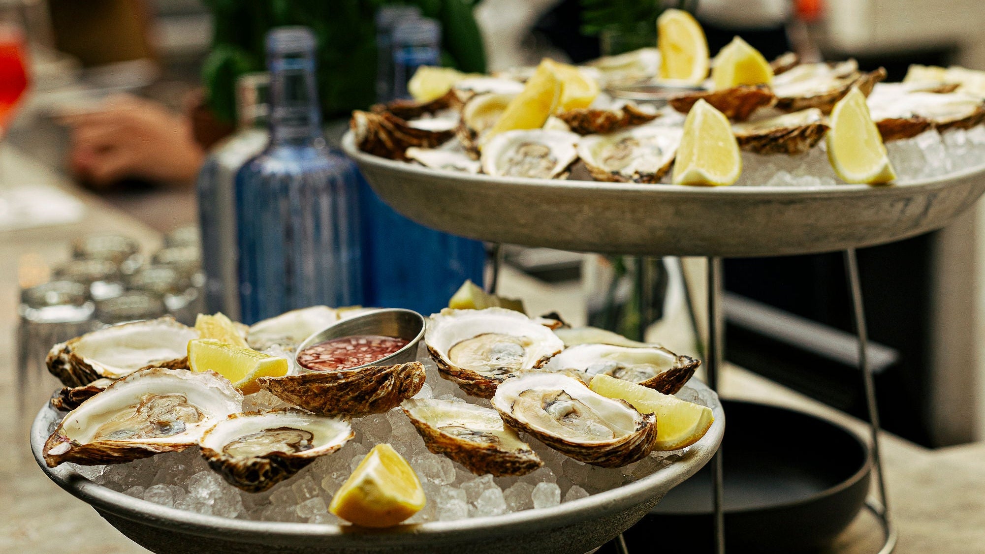 Oysters on a half shell with lemon wedges on a tiered stand in a restaurant setting.
