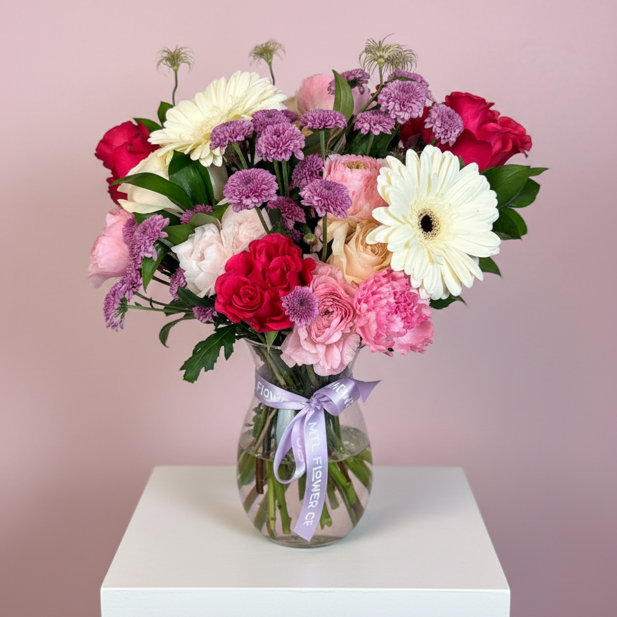 Bouquet of colorful flowers in a clear vase with a pink ribbon on a white pedestal against a pink background