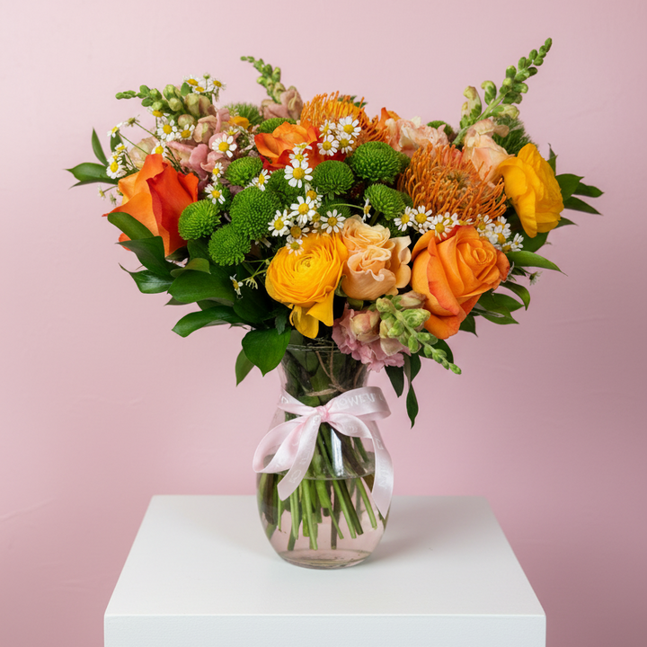 Bouquet of flowers in a clear vase with a pink ribbon on a white pedestal against a pink background