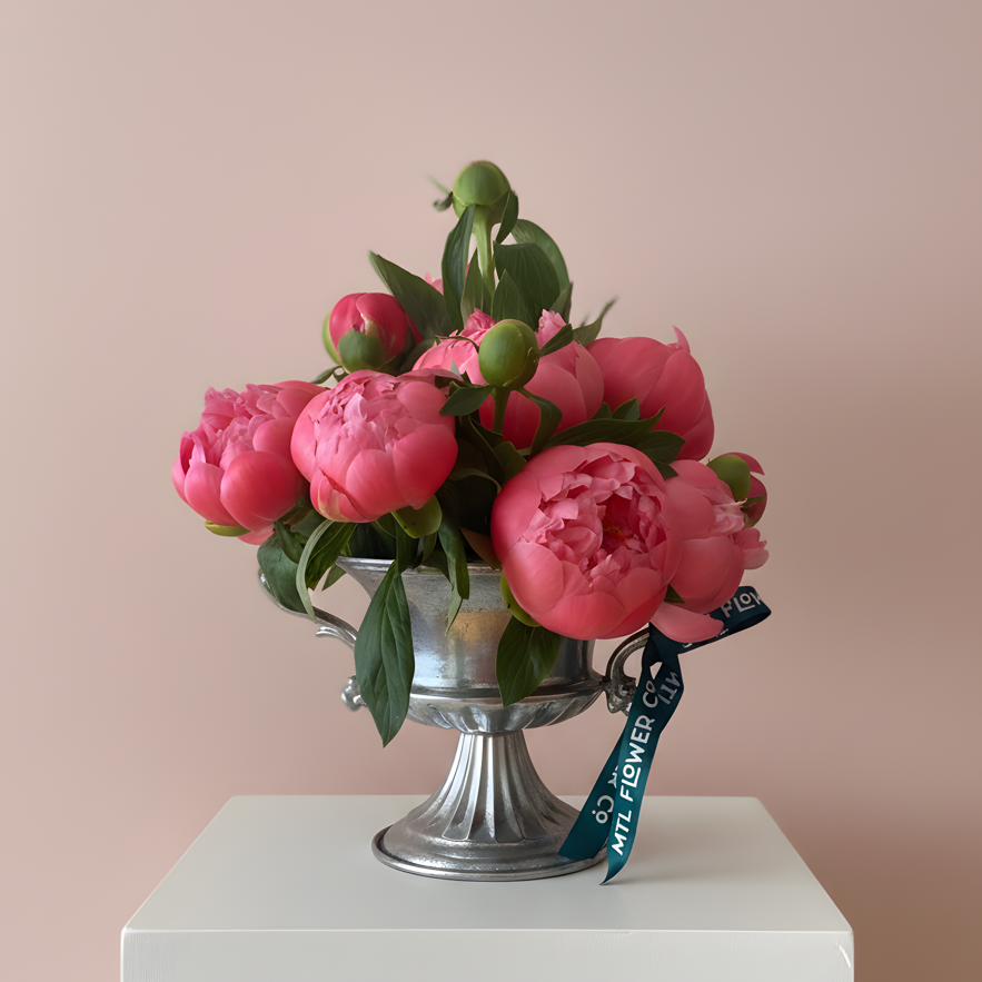 Bouquet of pink flowers in a silver vase on a white pedestal with a pink background