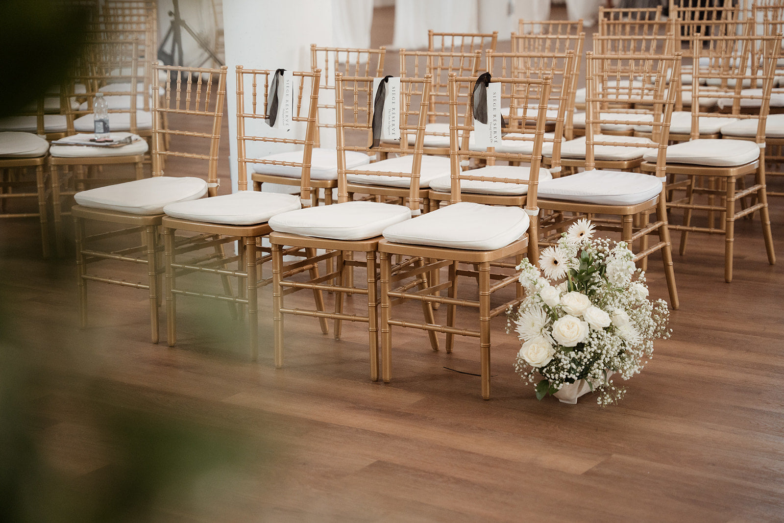 Decorated wedding venue with wooden chairs and floral arrangements on a wooden floor.