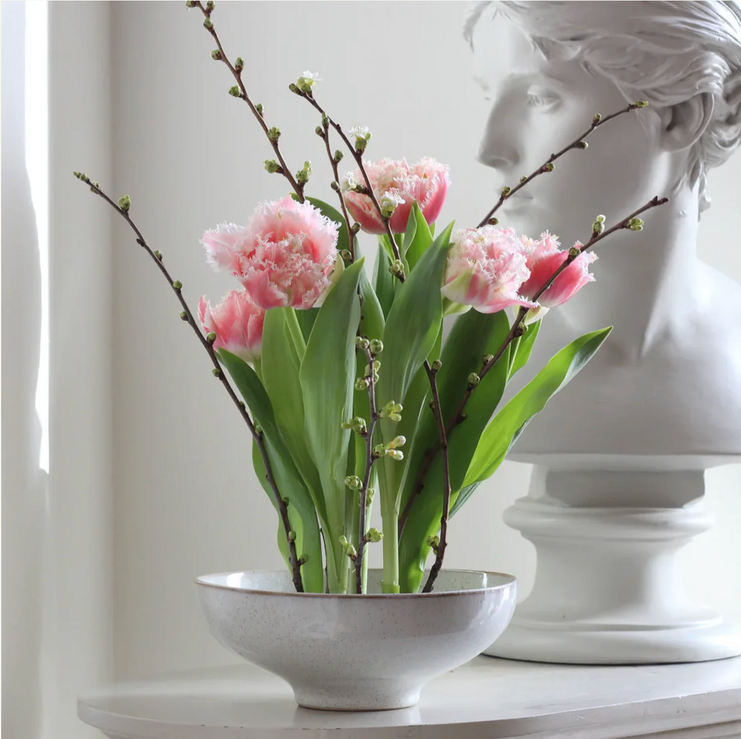 Bouquet of pink tulips in a white bowl with a classical statue in the background