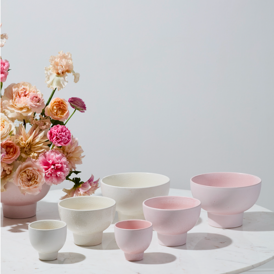 Set of ceramic bowls and a vase with flowers on a light surface.
