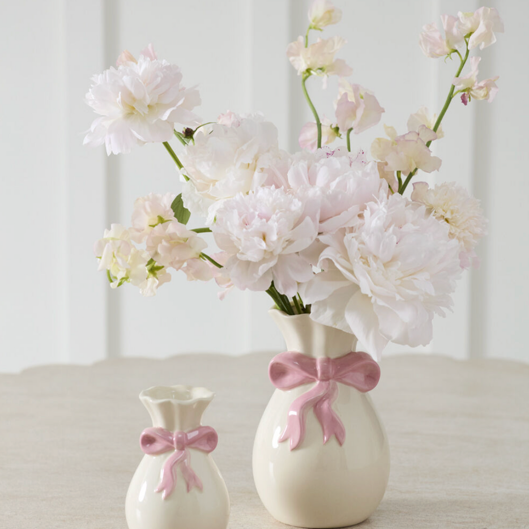 Two small white vases with pink bows on a light surface.