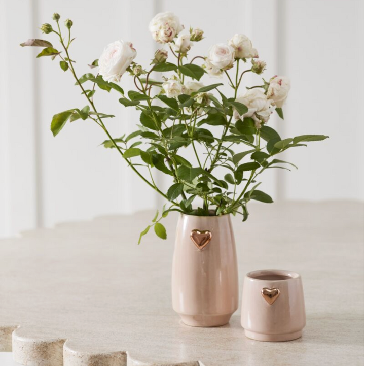 Two small ceramic vases with heart designs on a white surface, one containing flowers.