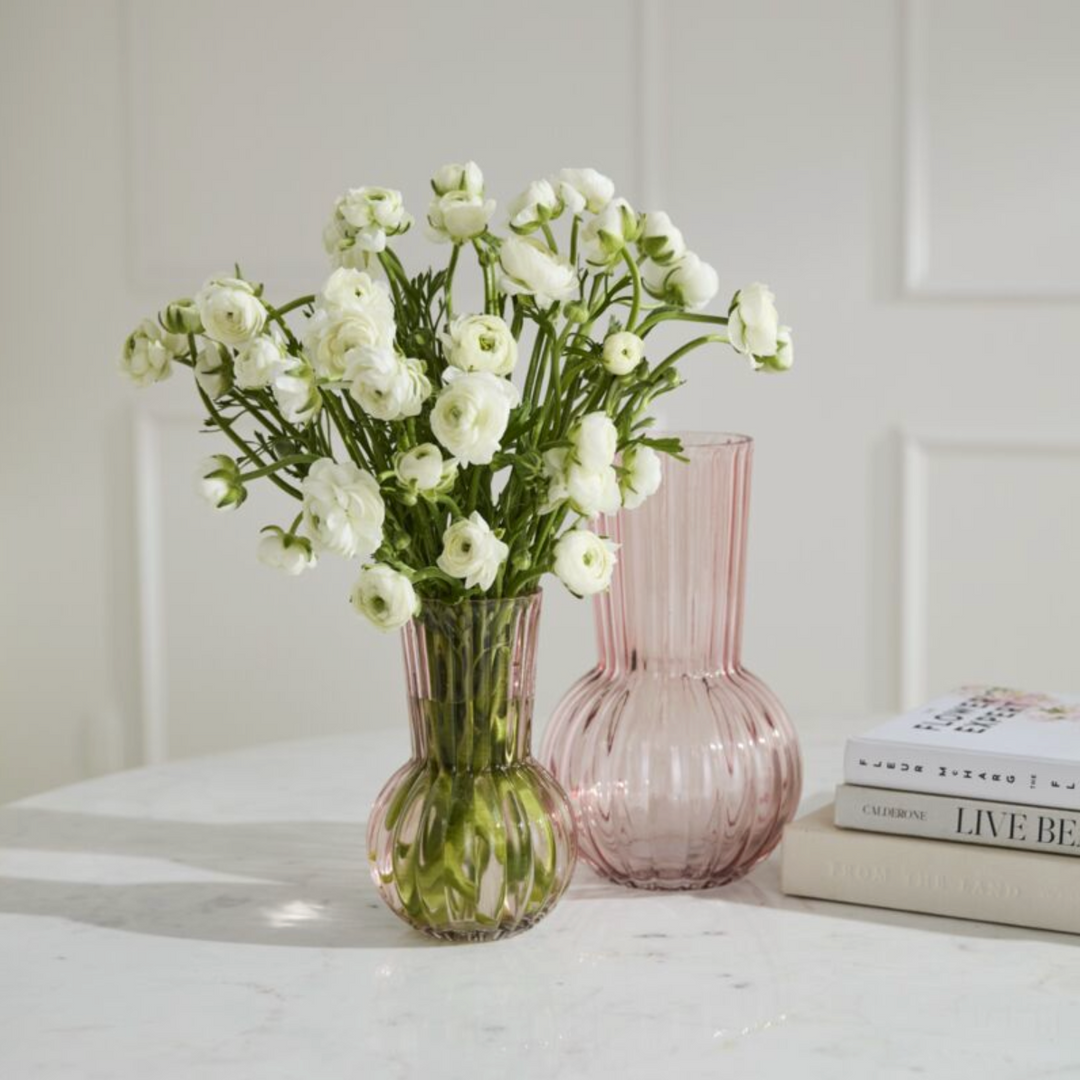 Two vases with white flowers on a light surface against a white wall