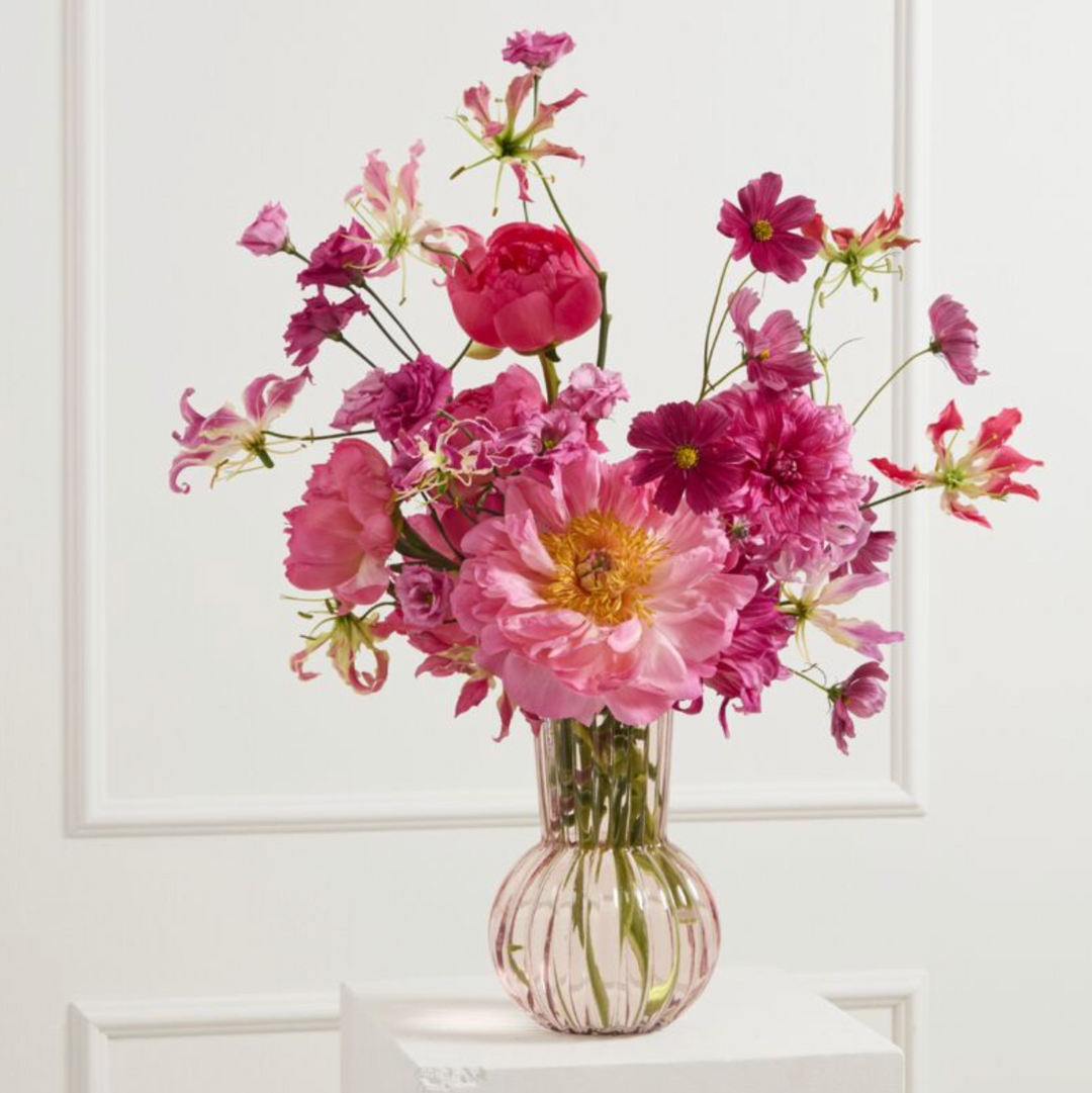 Bouquet of pink flowers in a clear vase on a white surface with a white background