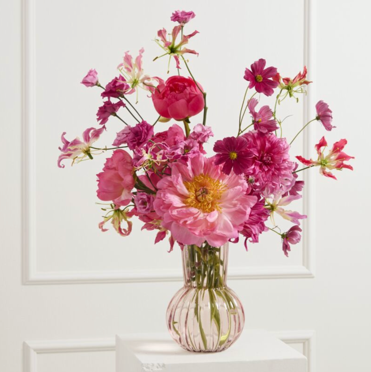Bouquet of pink flowers in a clear vase on a white surface with a white background