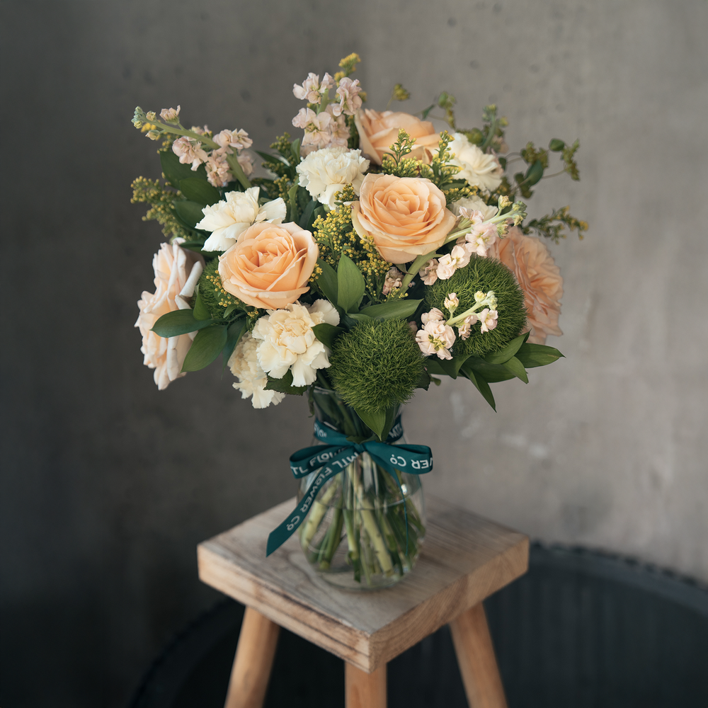 Bouquet of flowers in a glass vase on a wooden stool with a gray background