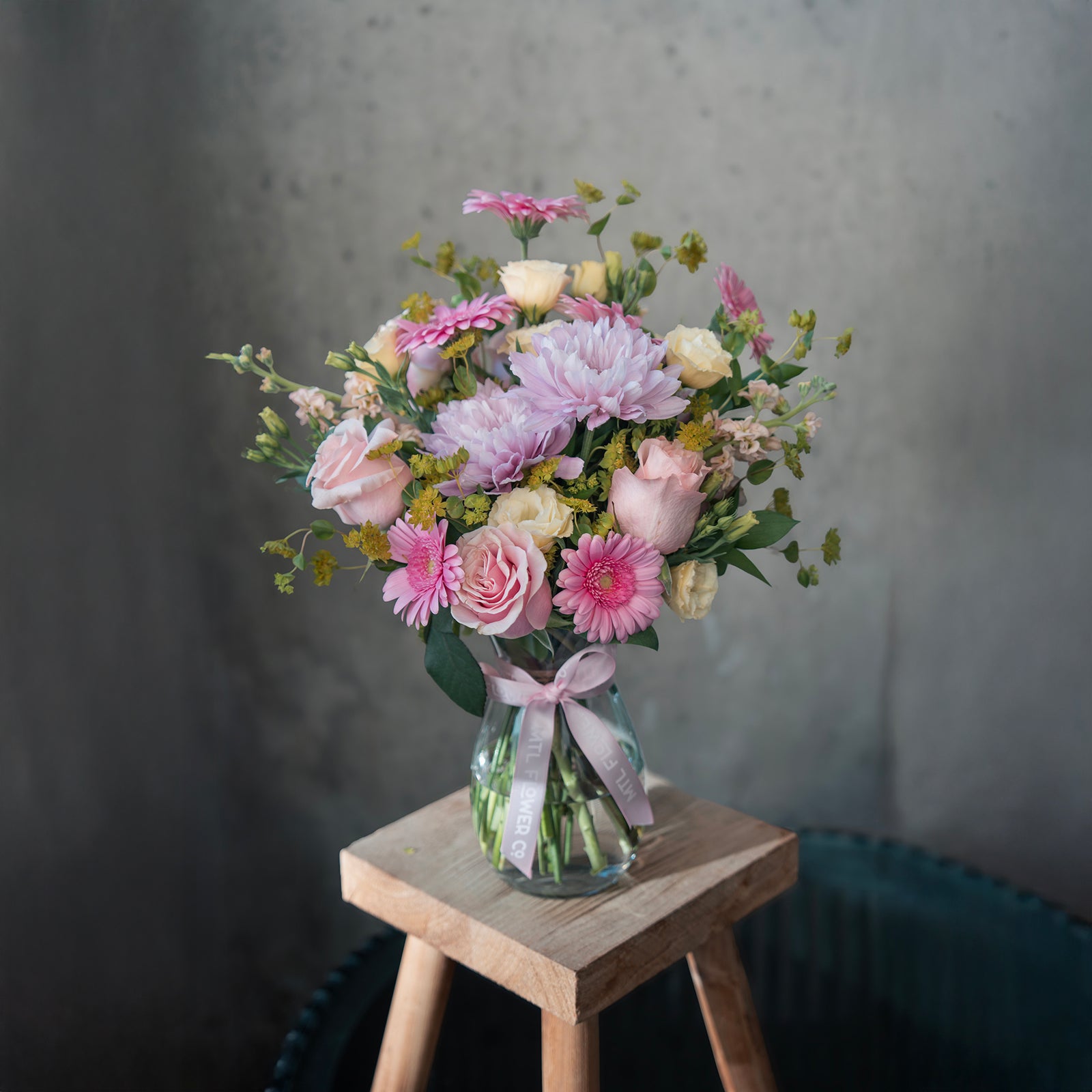 Bouquet of flowers in a glass vase on a wooden stool against a gray background