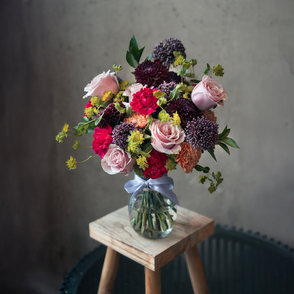 Bouquet of flowers in a clear vase on a wooden stool with a gray background